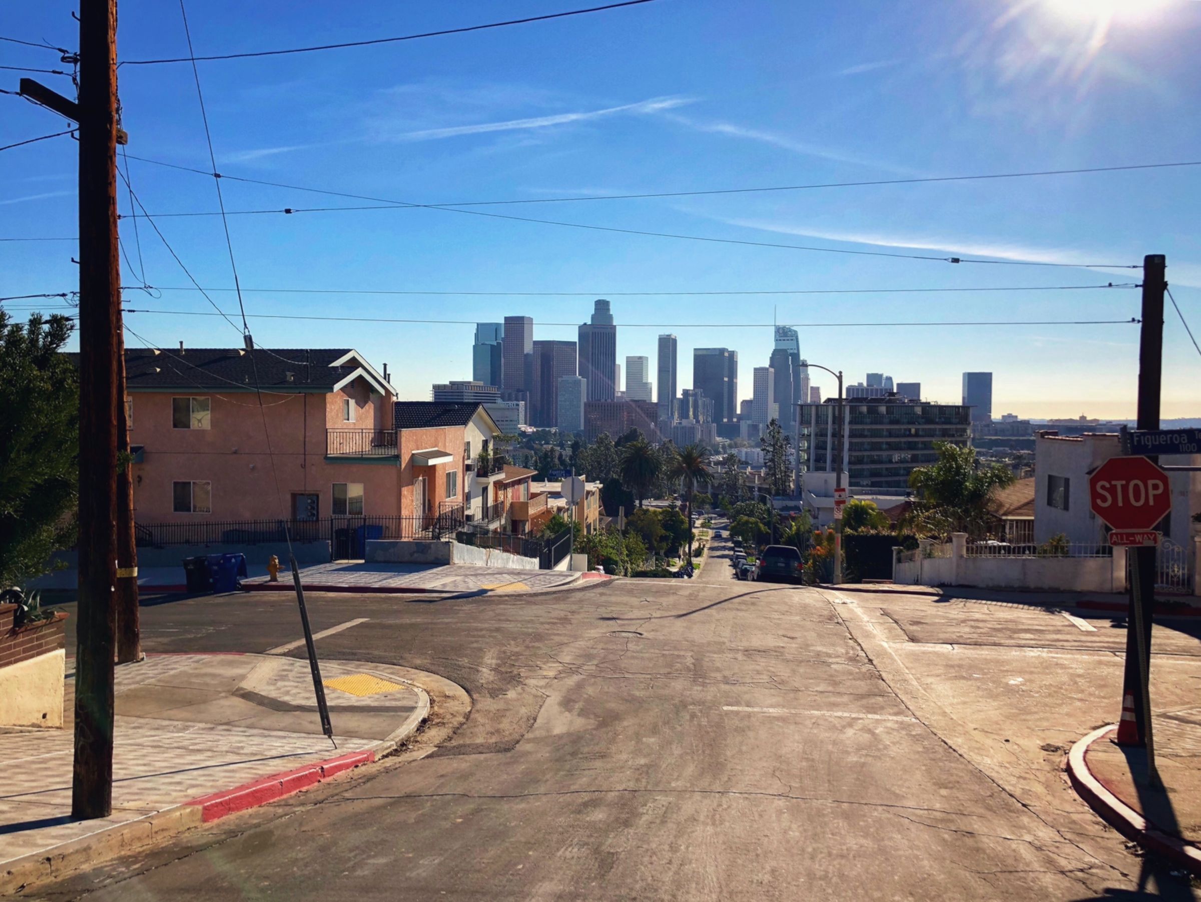 A steep residential street on Figueroa with the Downtown skyline framed between power lines