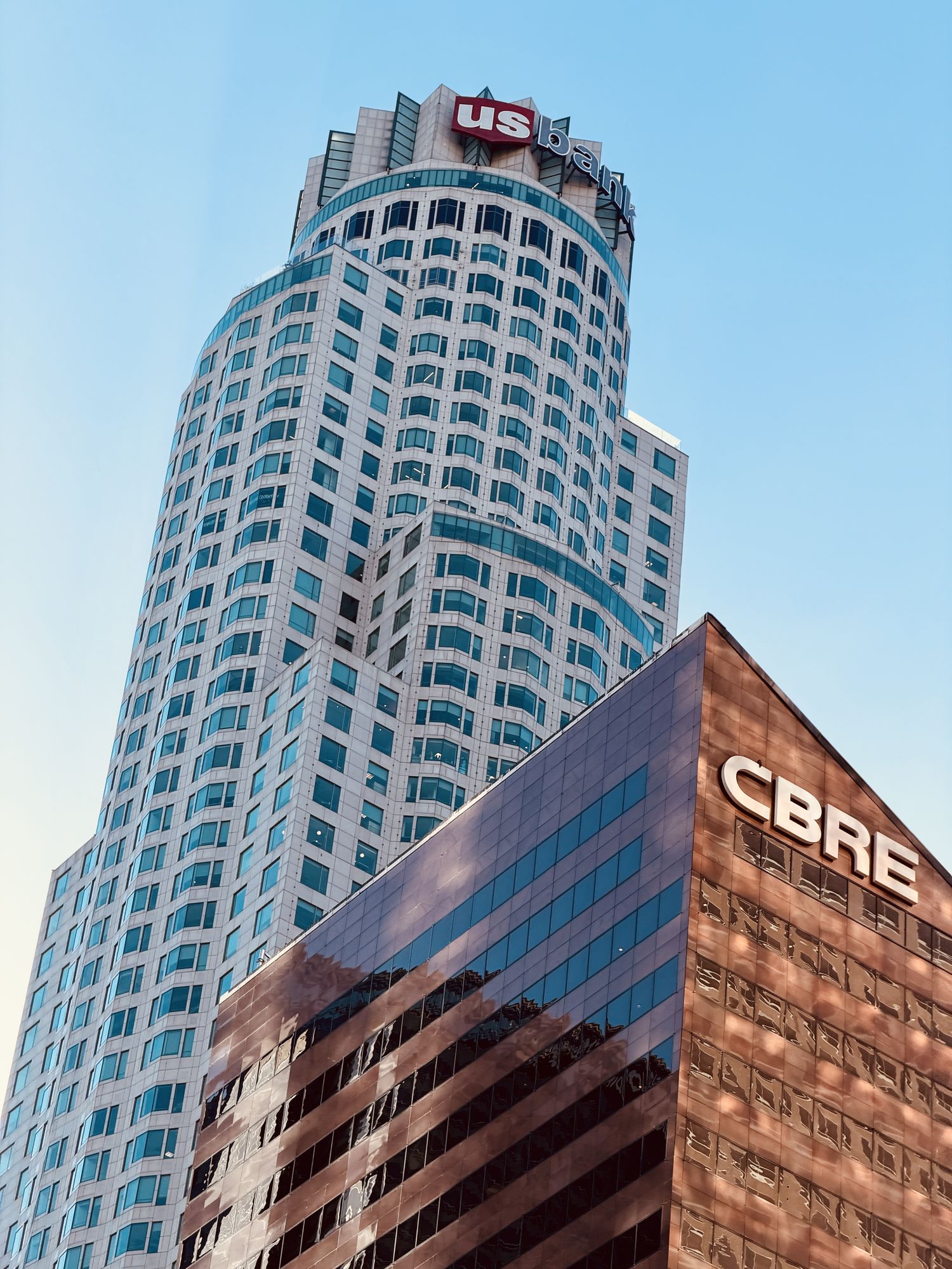 A rounded white skyscraper rising behind a copper-glass office block