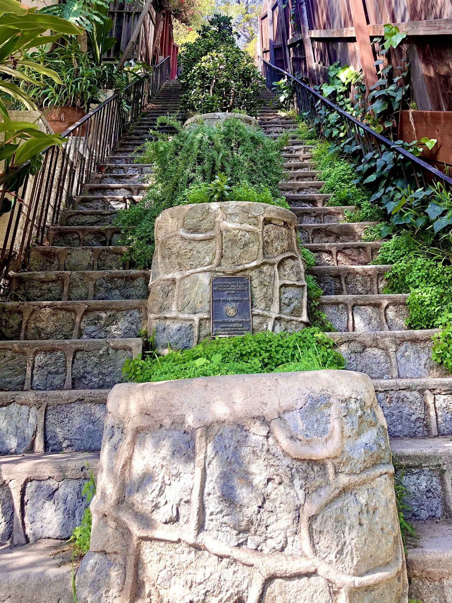 A flight of old granite steps climbing between gardens and wooden fences, with a heritage plaque on the stone landing